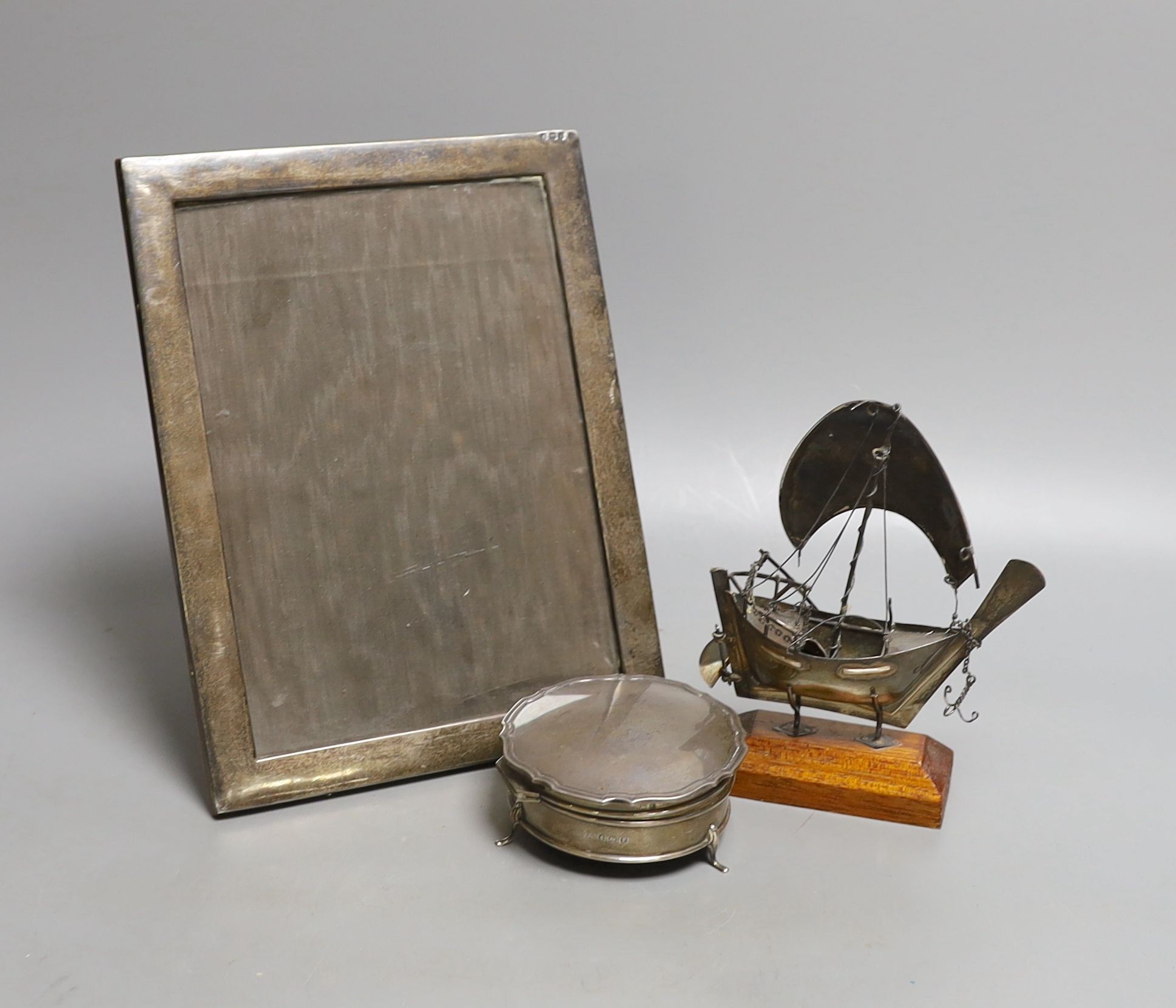 A George V silver mounted rectangular photograph frame, 24.2cm, a 1930's silver trinket box and a miniature white metal model of a sail boat, on wooden stand.